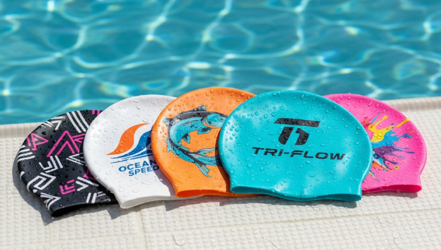 Custom printed silicone swim caps in various colors and designs with team logos and creative graphics by a pool.