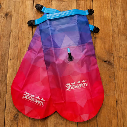 Flotador de natación rojo y morado con correas azules sobre una superficie de madera, con la marca '360swim'.